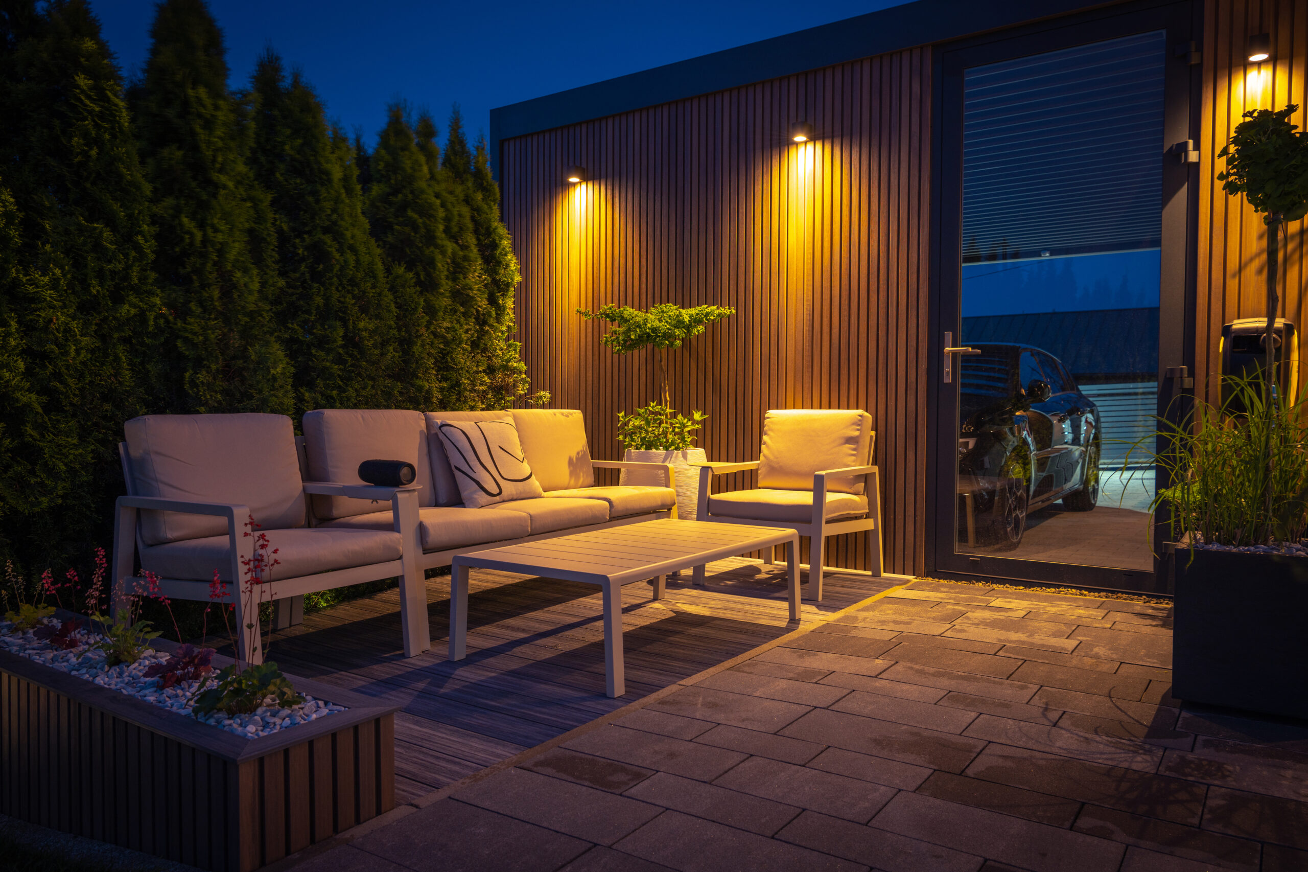 Lounge and Dining Area at Modern Residential Backyard Decorated with Outdoor Lights, Plants, Garden Table and Chairs. Cozy Summer Evening.